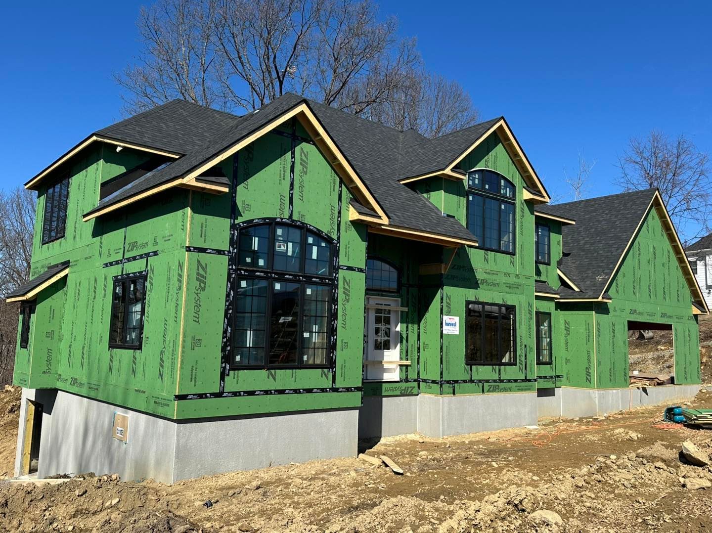 A house under construction with green wrap, dark roof, and windows.
