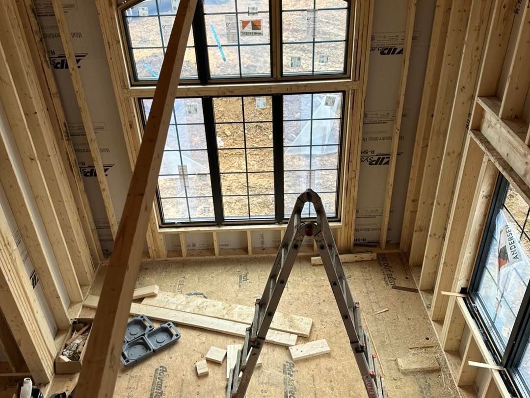 Interior view of a building under construction, featuring a tall window frame and ladder.
