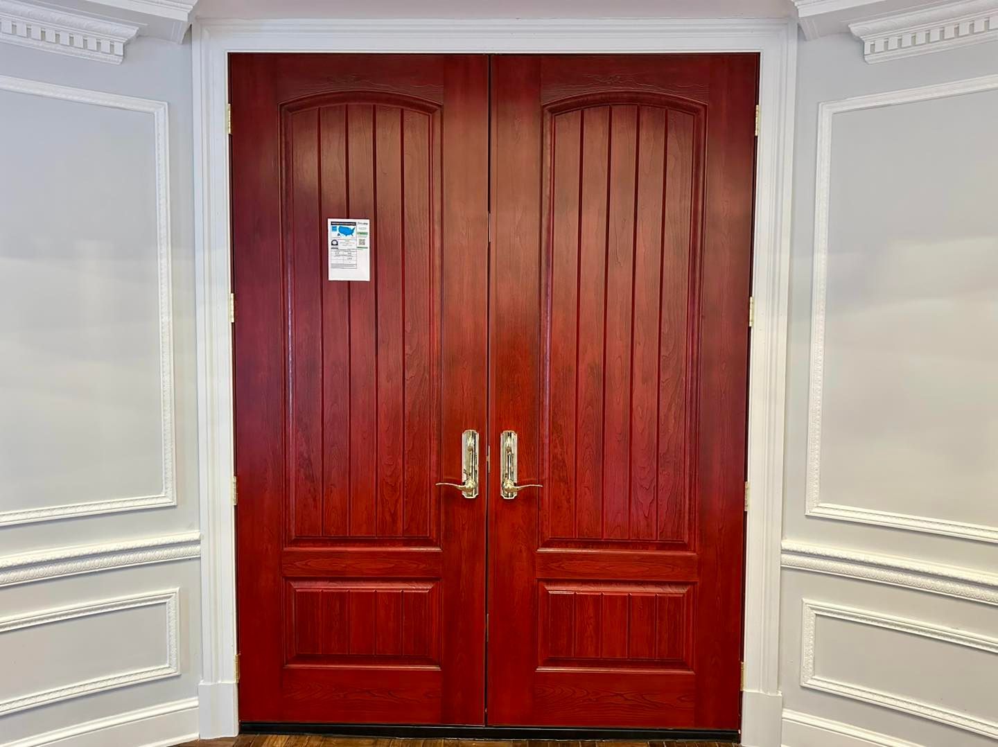 Red double doors with gold handles, set in white paneled walls.