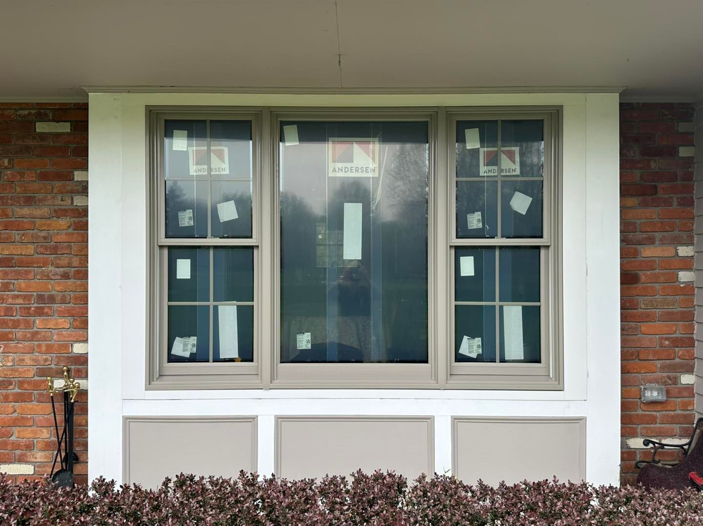 A three-pane window with brown frames, set in a white and brown facade against a brick wall.