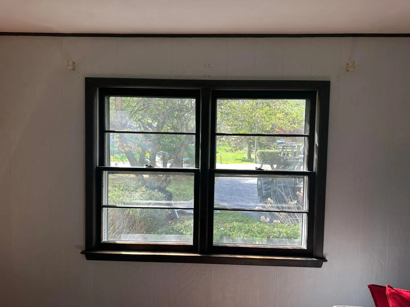 Black-framed window with six panes showing trees outside on a plain white wall