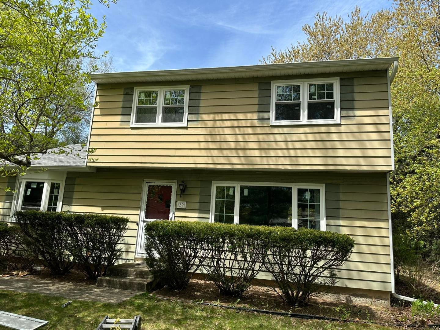 Two-story house with green siding, white-trimmed windows and shutters, and a red front door.
