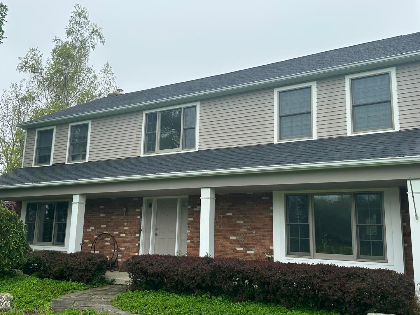 Two-story house with brick base, tan siding, dark roof, white trim, and a porch.