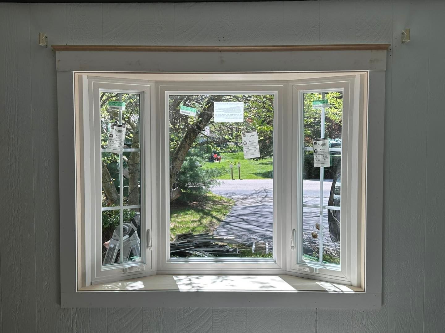 Bay window with three panes, white frame, open side windows, overlooking a tree-lined path.