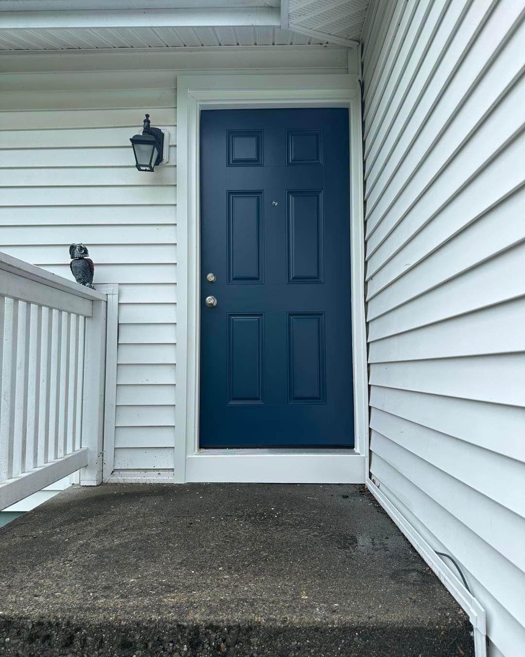 Dark blue door with white trim set in white siding, front porch view.