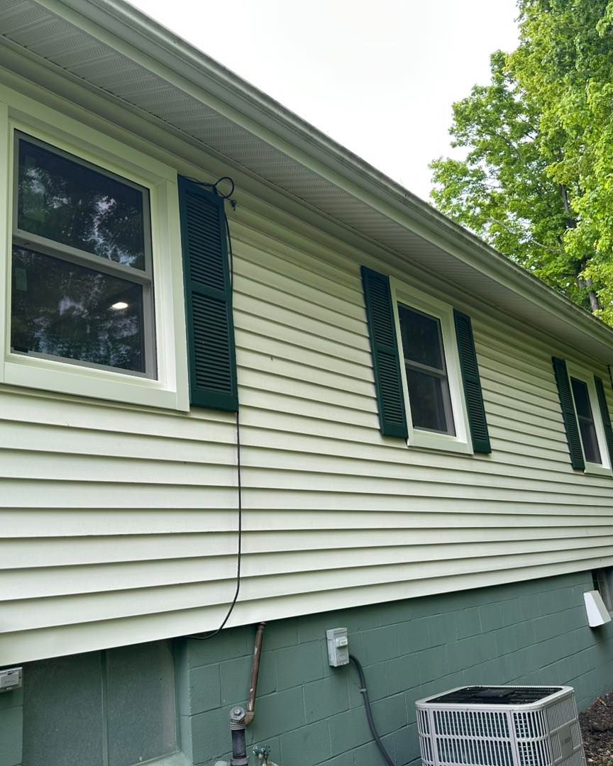 Side of a house with light green siding, dark green shutters, and a dark green foundation.