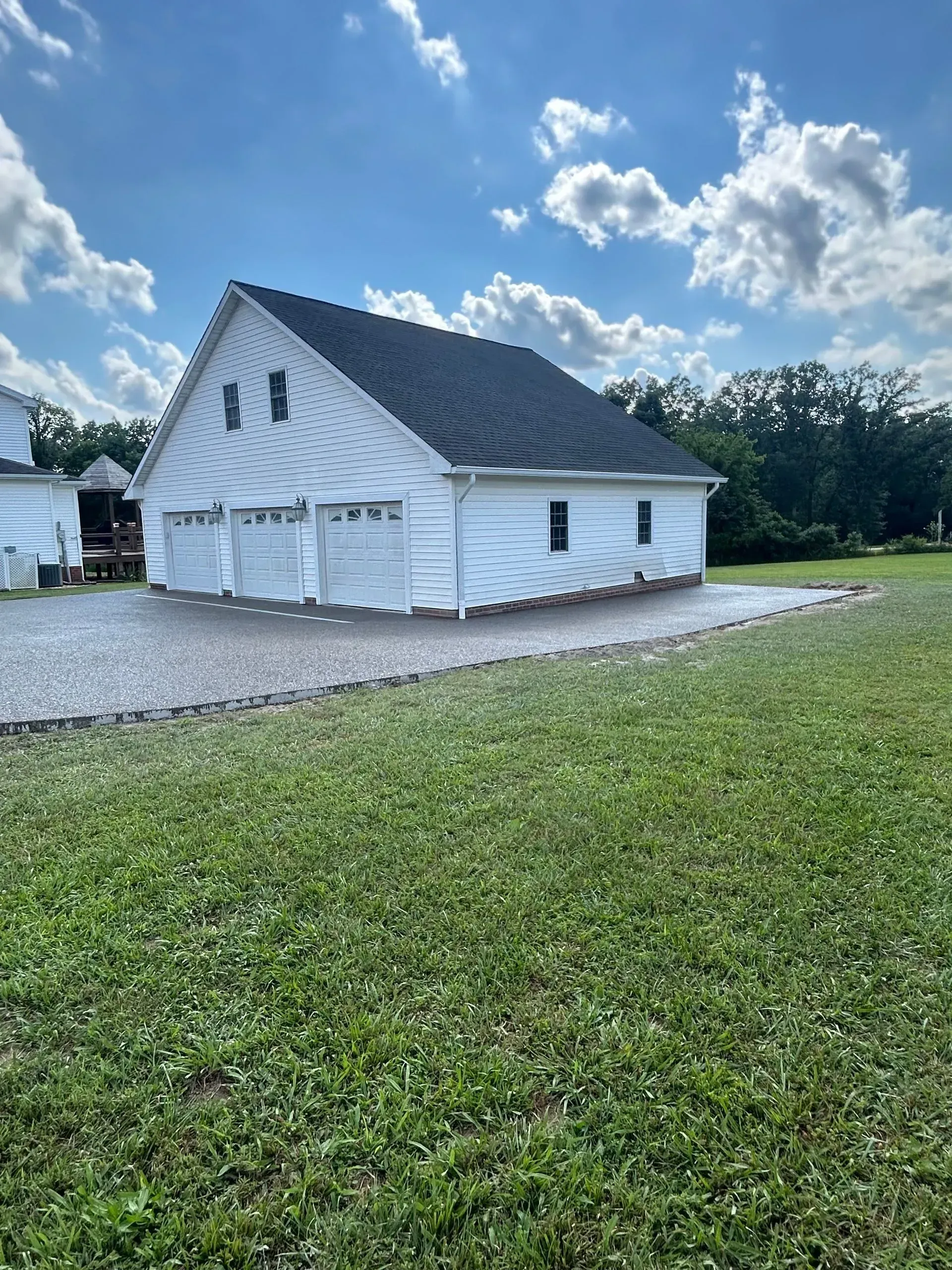 White building with dark roof on a gravel lot under a cloudy blue sky