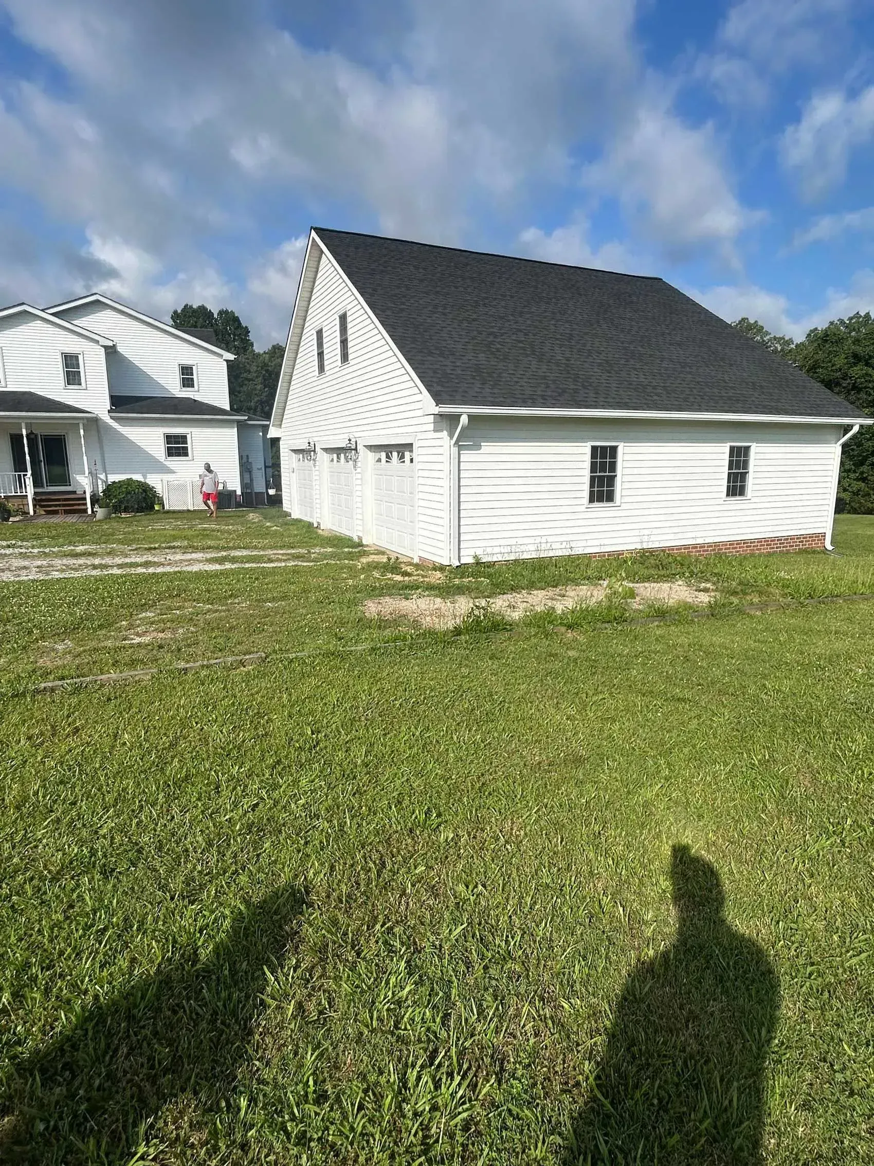 White house and small outbuilding on a grassy lot under a blue sky with clouds
