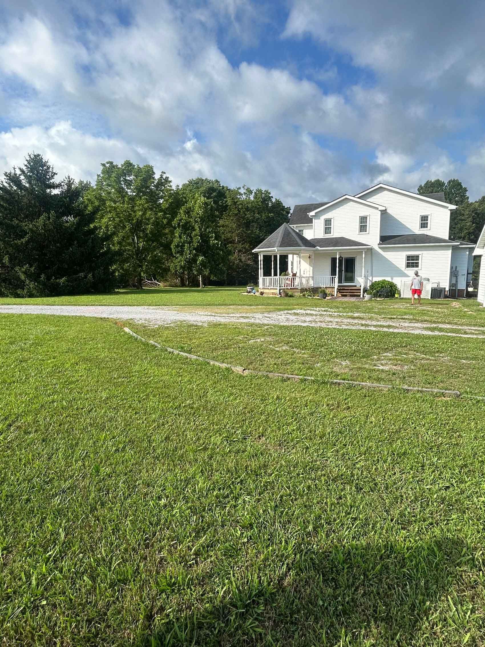 White farmhouse with porch beside a grassy field under a blue sky with clouds