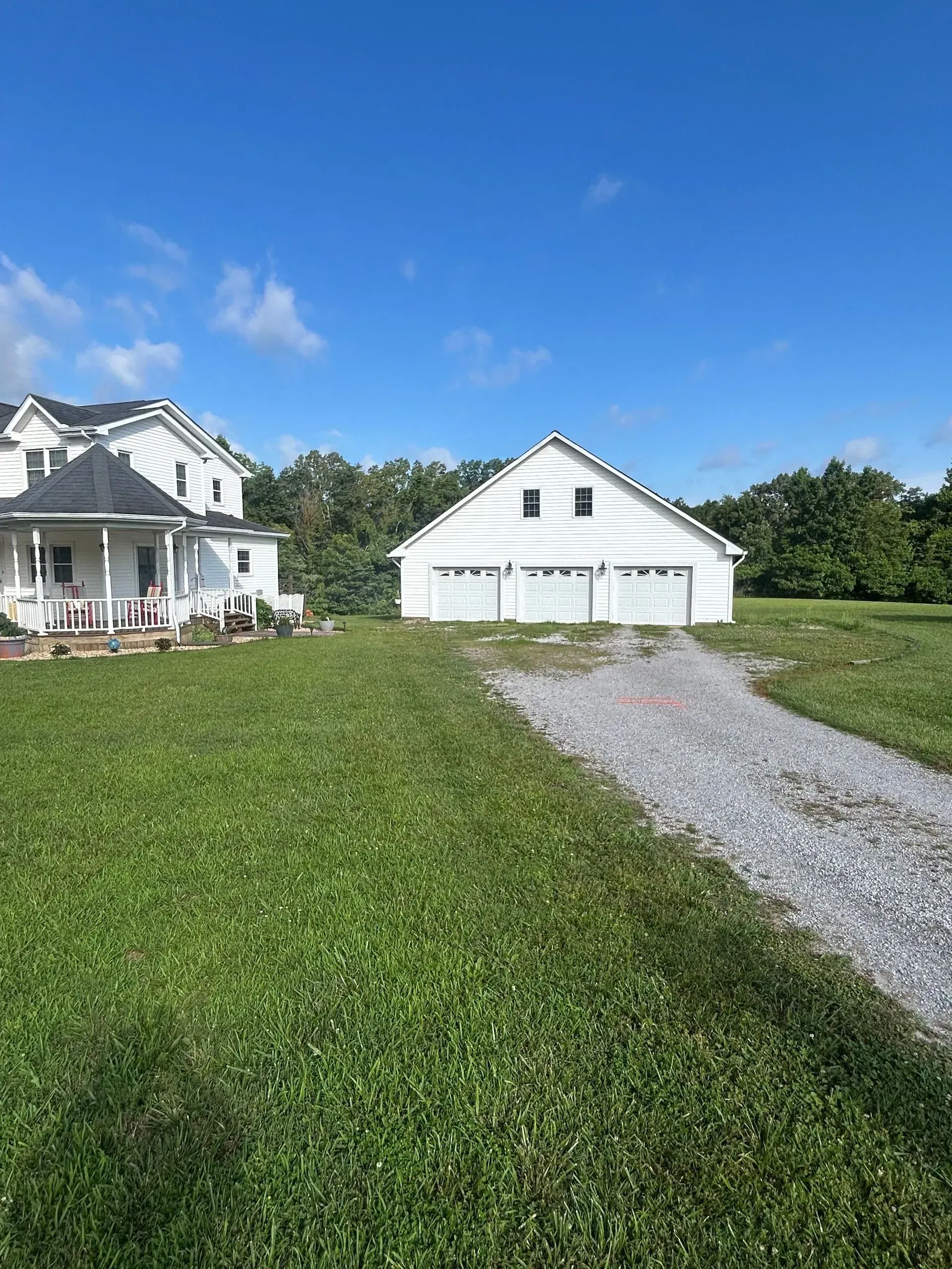 White house and garage beside a gravel driveway under a bright blue sky, with a grassy lawn in front