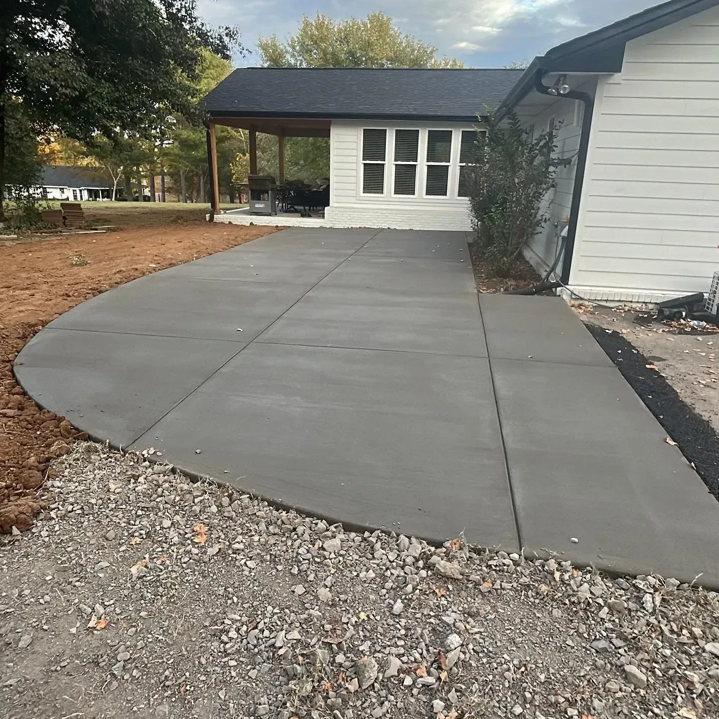 Concrete driveway leading to a white house with a covered porch and gravel edging