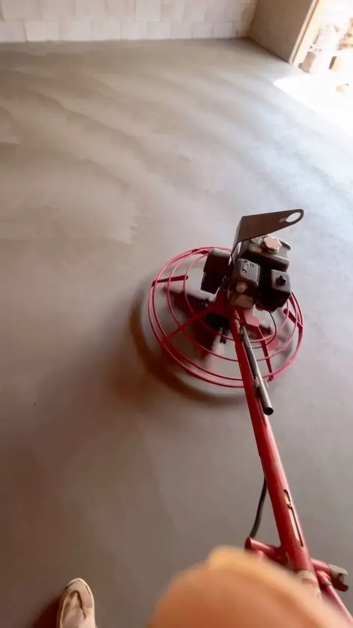 Person using a red floor polisher on a smooth gray floor inside a room