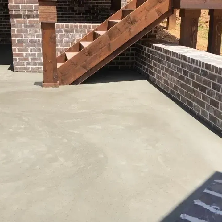 Concrete patio beside brick wall and wooden stairs with railing in sunlight