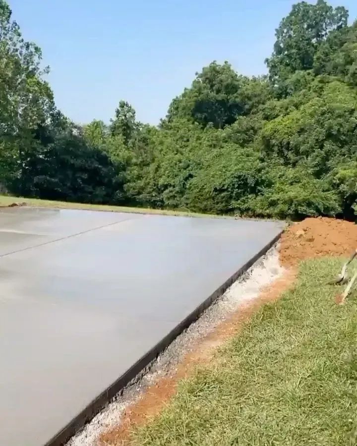 Freshly poured concrete slab beside a grassy slope and dense green trees