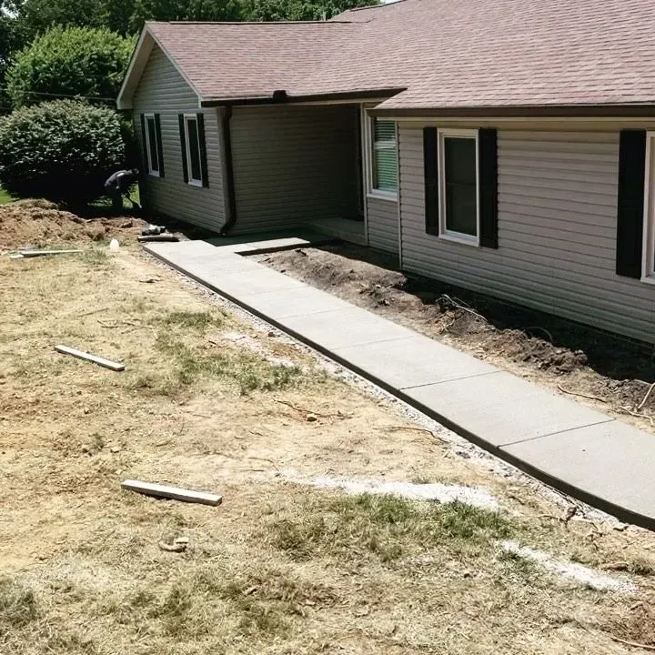 Concrete sidewalk beside a beige house with a brown roof, crossing a dry, patchy lawn