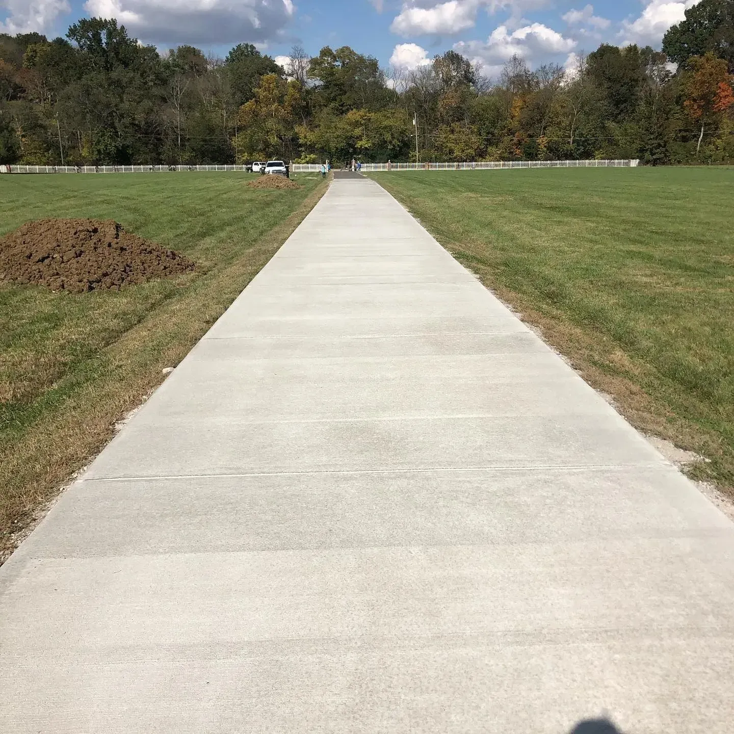 Concrete path through a grassy park toward trees under a partly cloudy sky