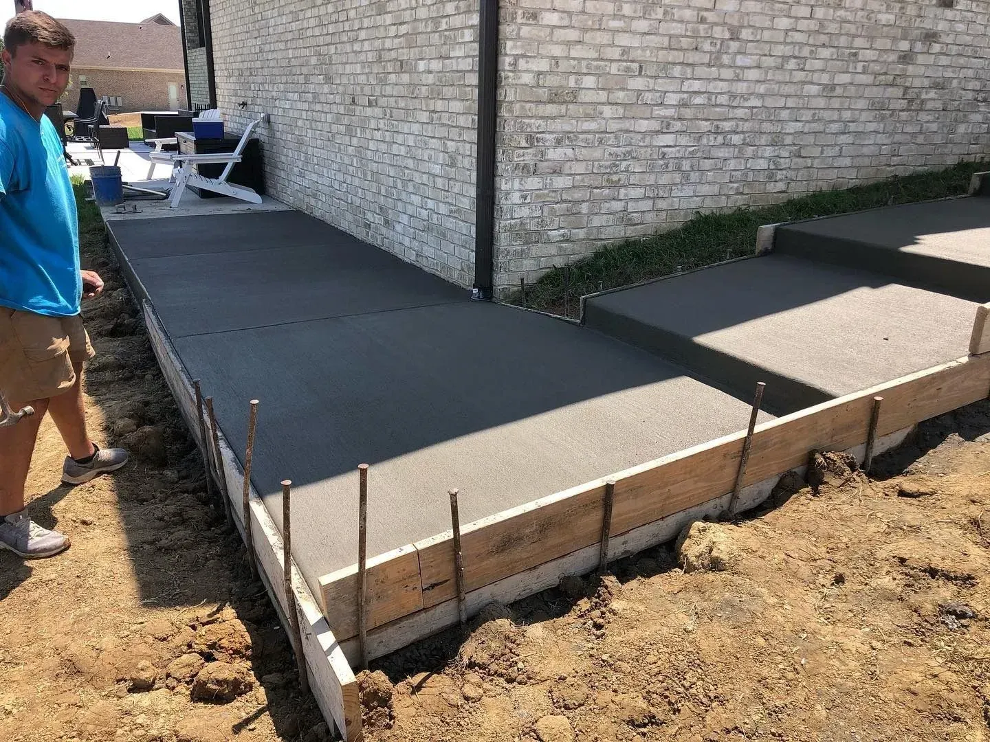 Covered porch with wet stamped concrete floor, wooden posts, and a white door on a gray house