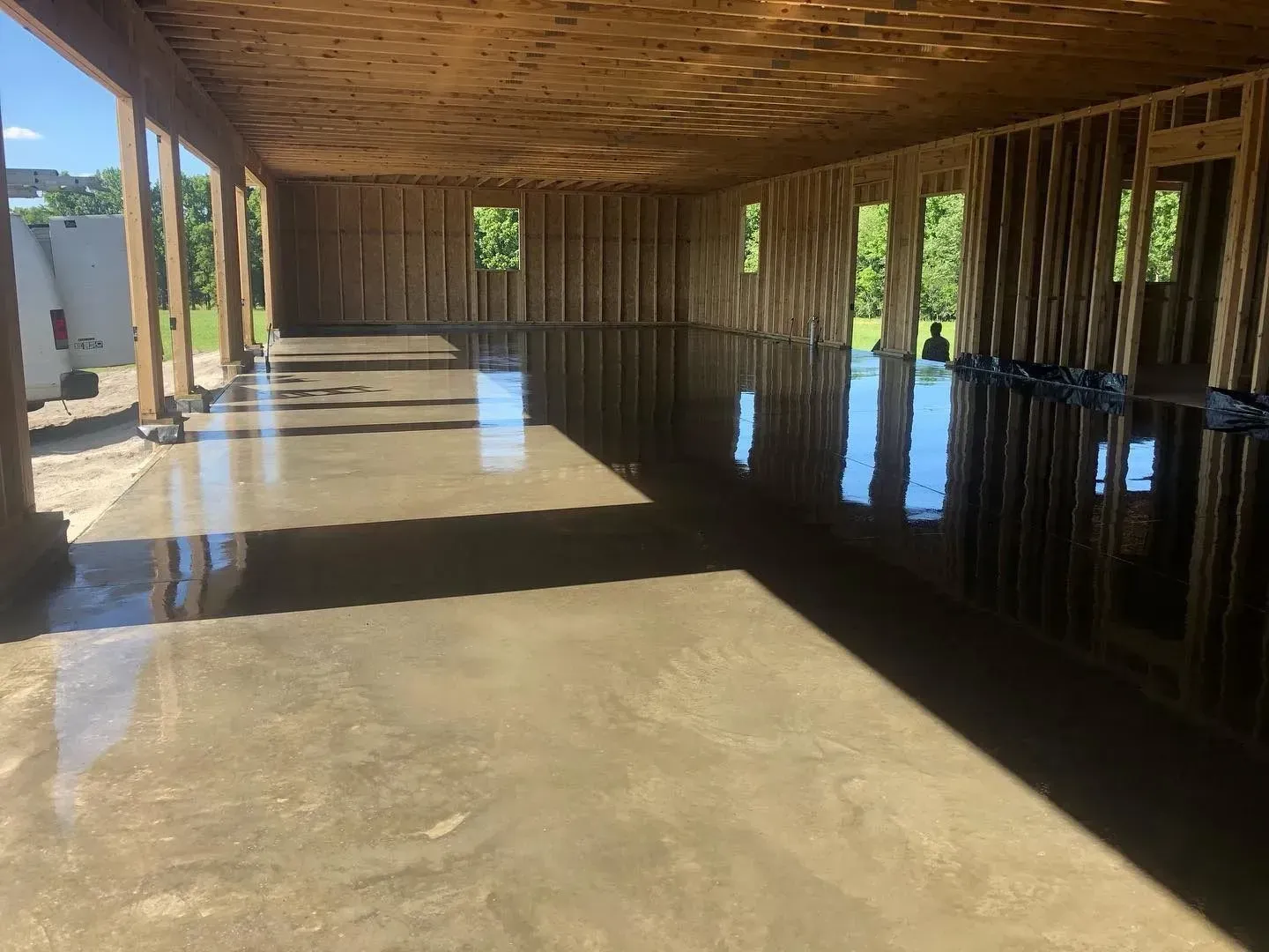 Empty covered corridor with wooden beams, concrete floor, and sunlight casting shadows through open sides