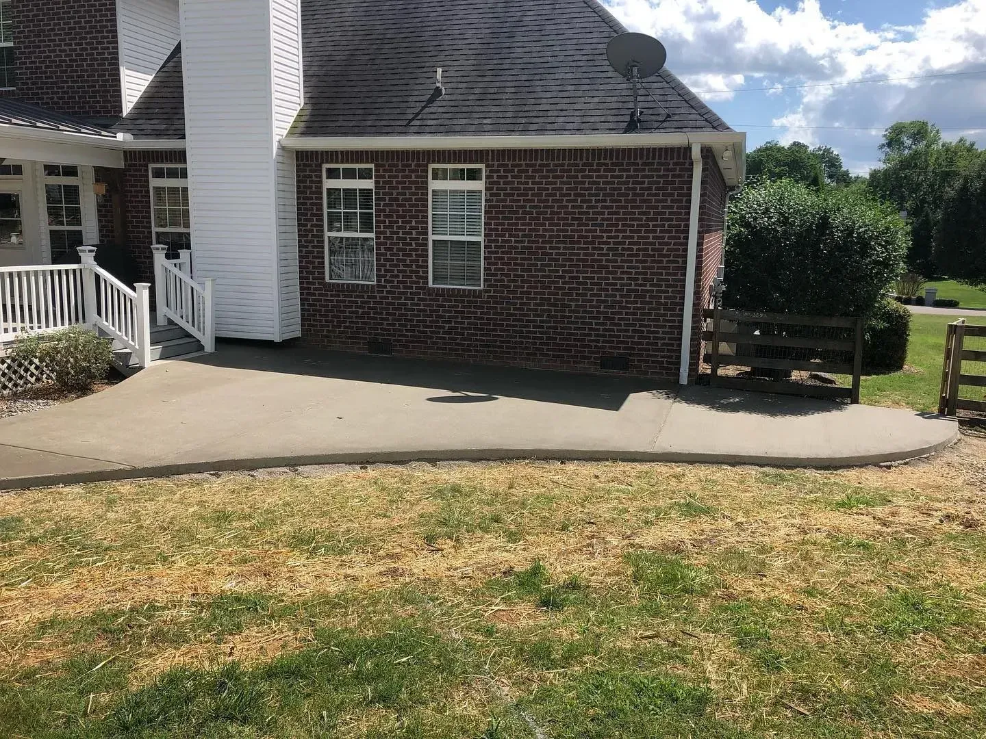 Brick house with a curved concrete patio and white railing, viewed from a grassy yard.