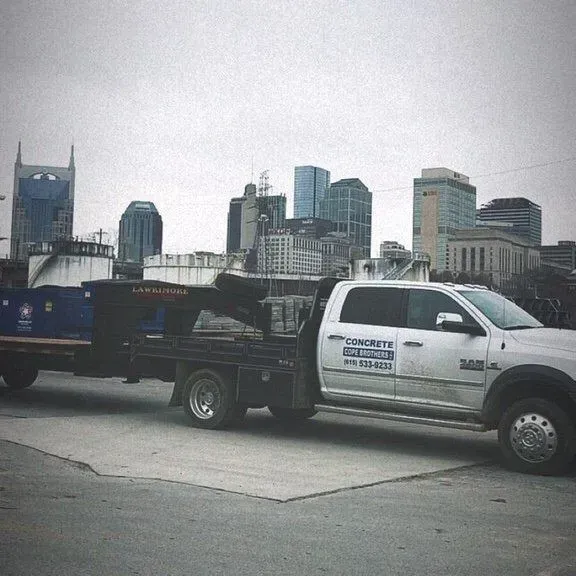 White pickup truck towing a black trailer in front of a city skyline under overcast skies