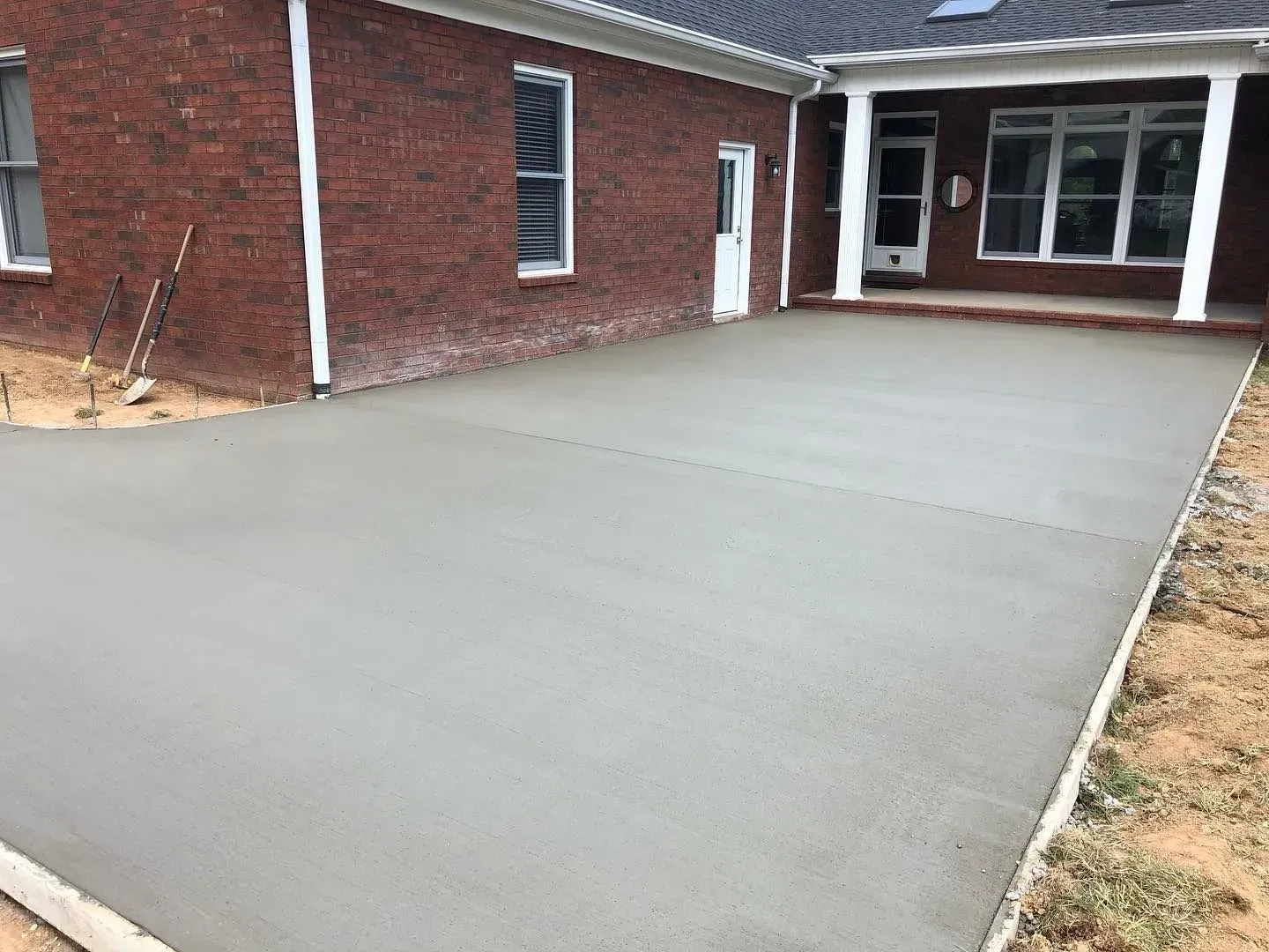 Fresh concrete patio beside a red brick house with a covered entryway