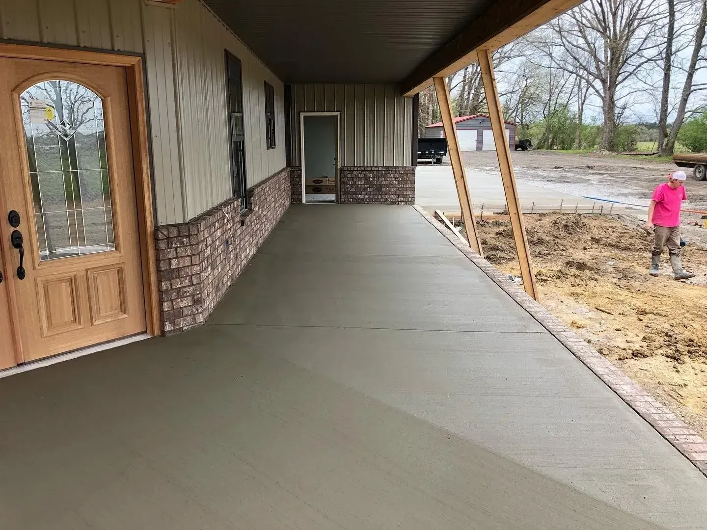 Curved concrete driveway beside a green lawn and trees, leading past a house in a wooded setting