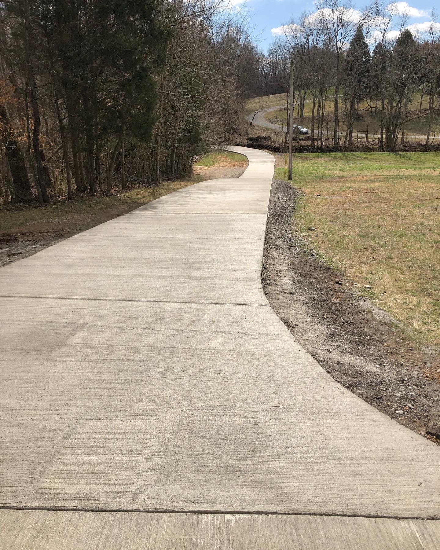 Curving concrete path through a grassy park with trees and a cloudy sky