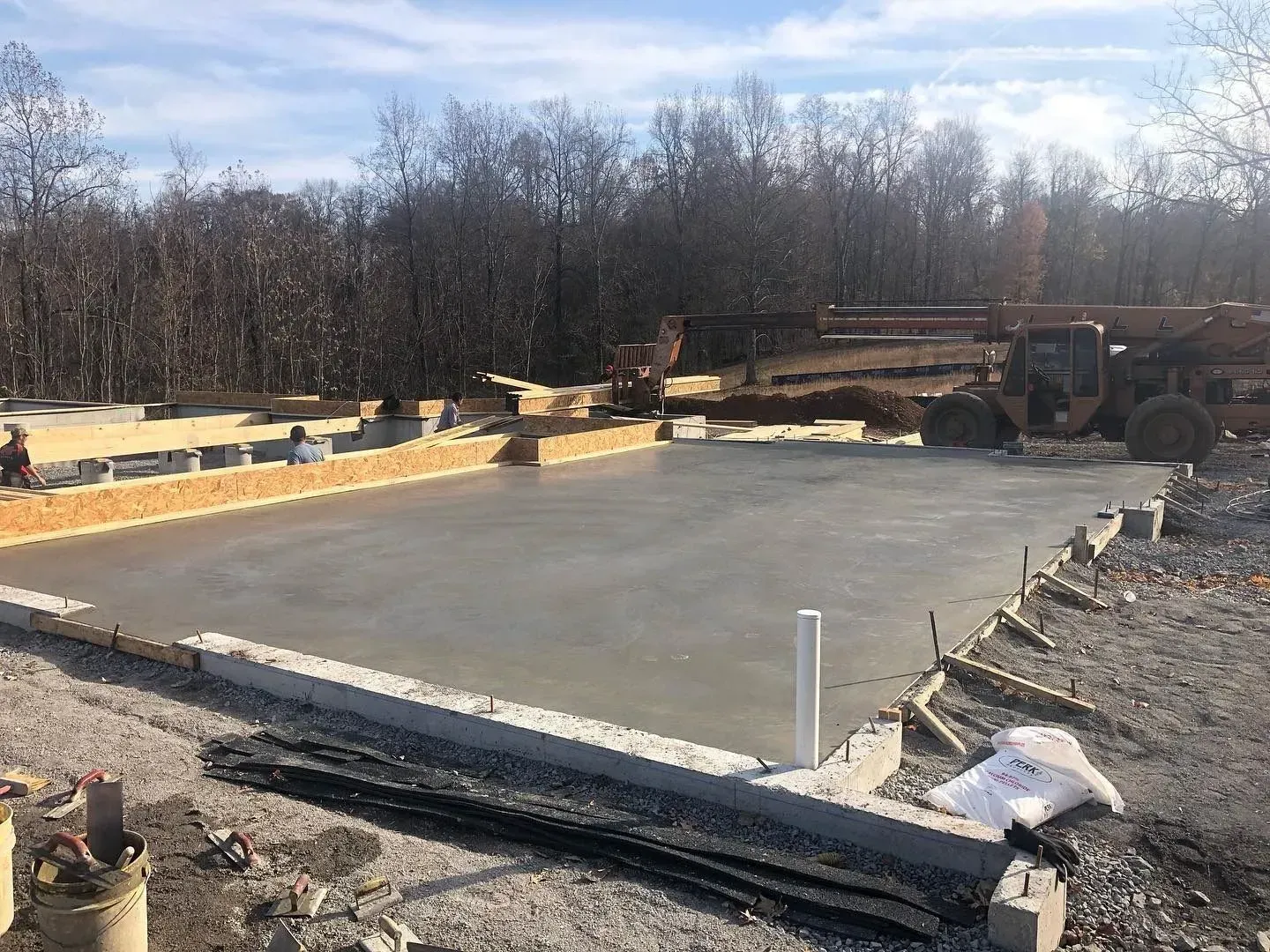 Concrete slab being poured on a construction site, with workers and heavy equipment in the background