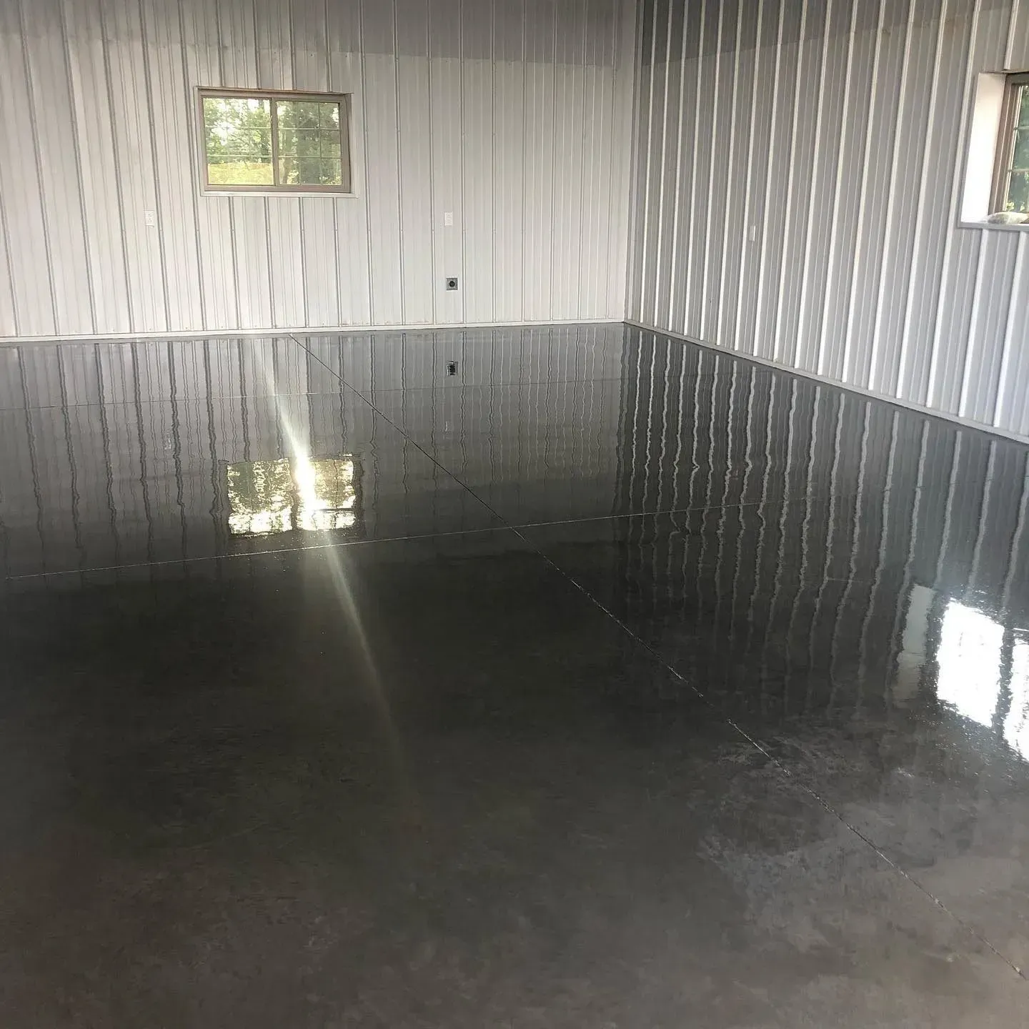 Empty room with dark glossy floor, corrugated metal walls, and two small windows.