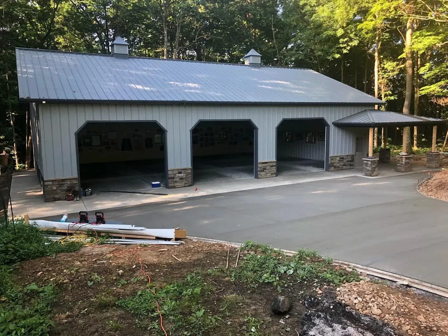Three-bay garage with a gray metal roof beside a wooded driveway at dusk