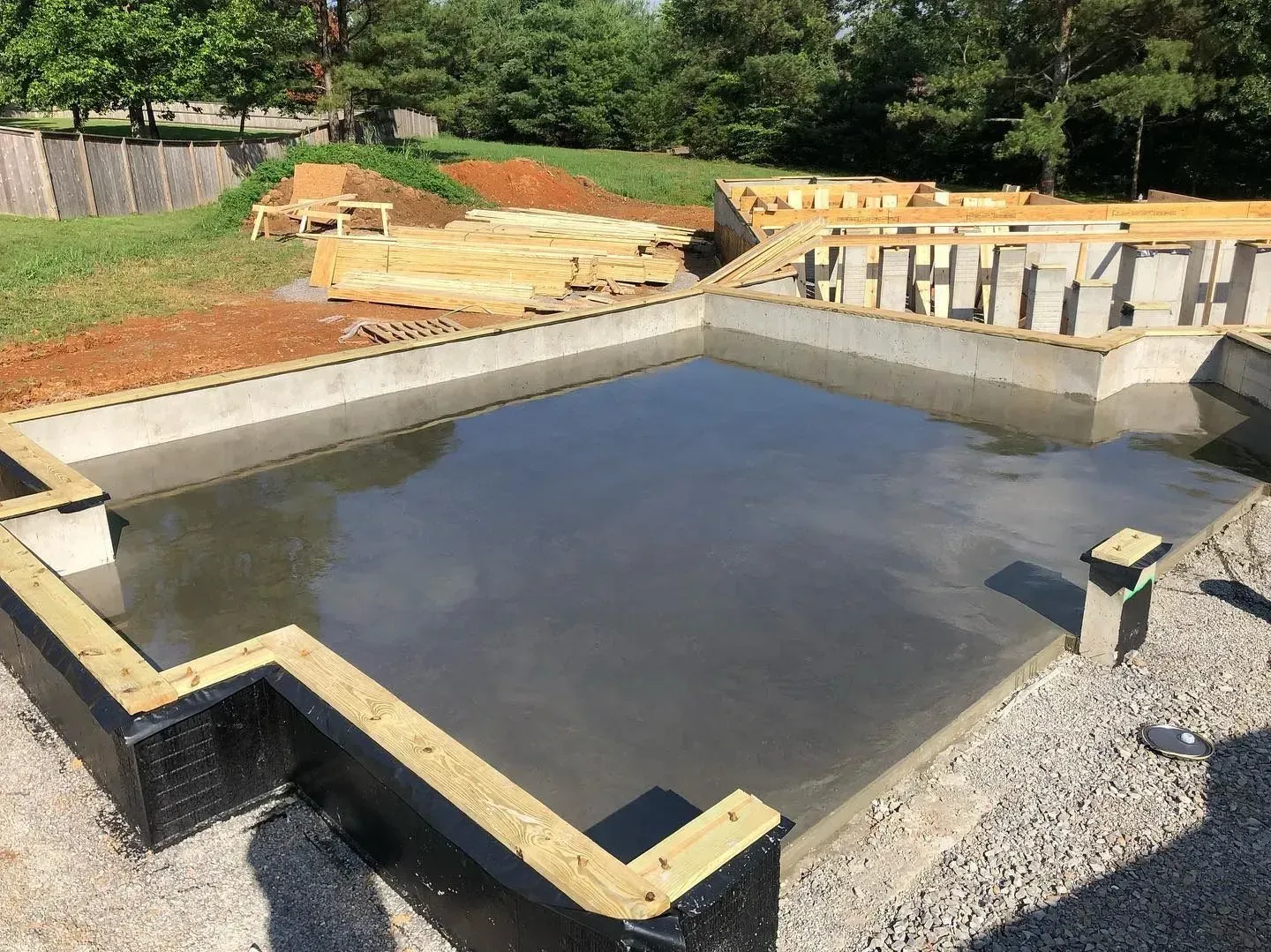 Concrete water basin under construction with dark water, gravel edges, and dirt embankments