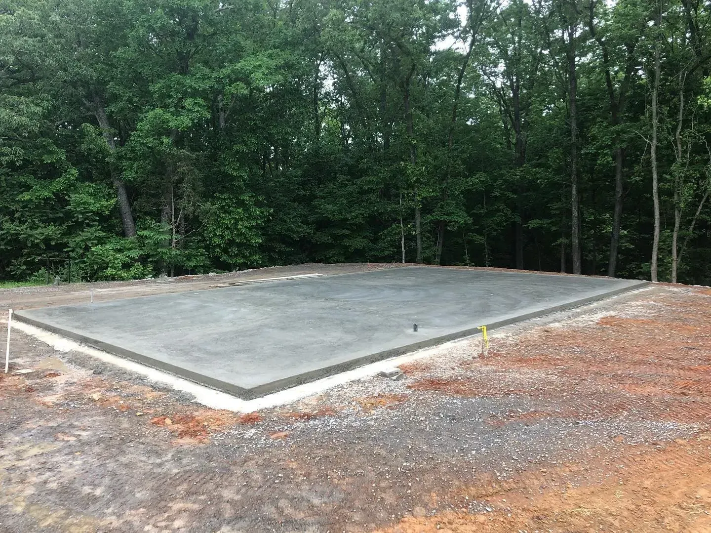 Concrete slab foundation in a wooded clearing with gravel around it