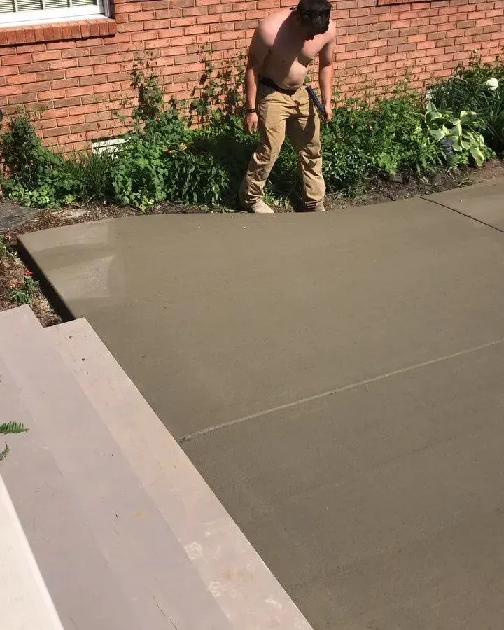 Worker smoothing fresh concrete beside a brick wall and garden bed