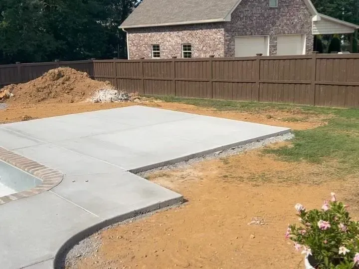 New concrete patio with curved edge beside a wooden fence and a house in a backyard