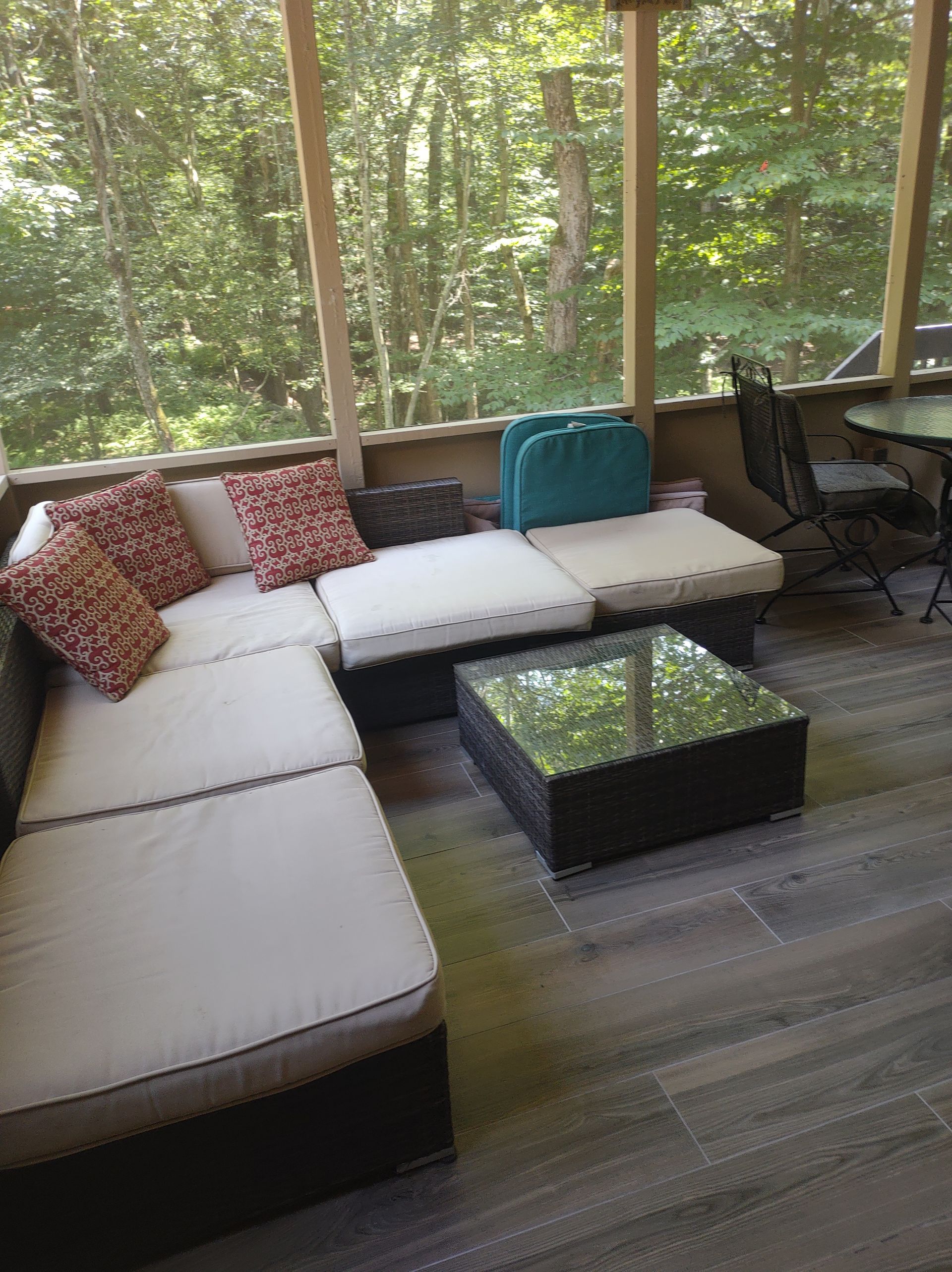 Screened-in porch with sectional sofa, square coffee table, and forest backdrop.