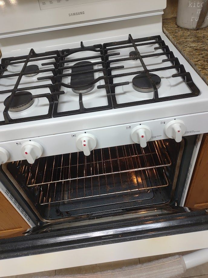 White gas stove with open oven door and black stovetop grates.