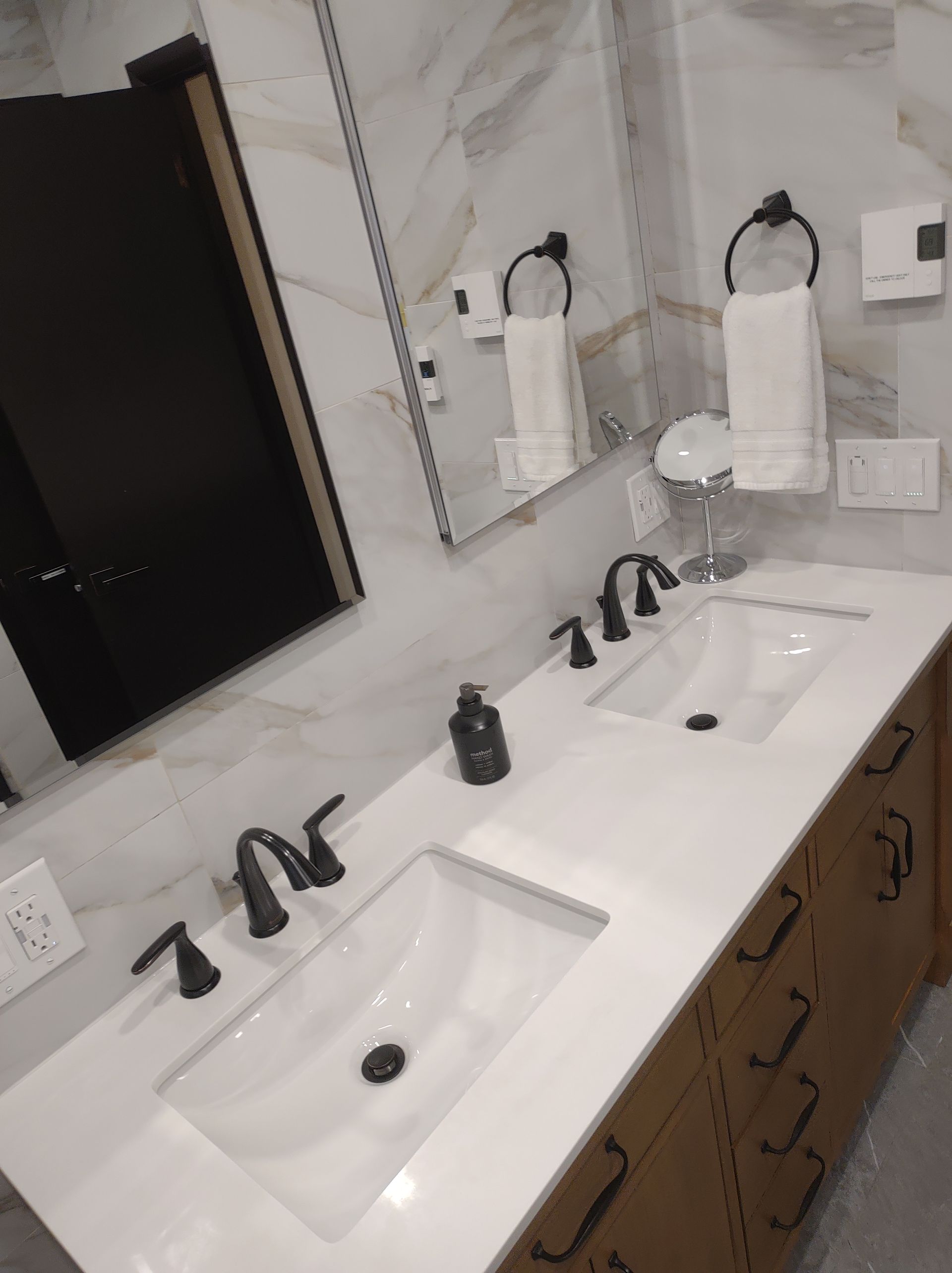 Bathroom with a double sink vanity, white countertop, black fixtures, and mirror.