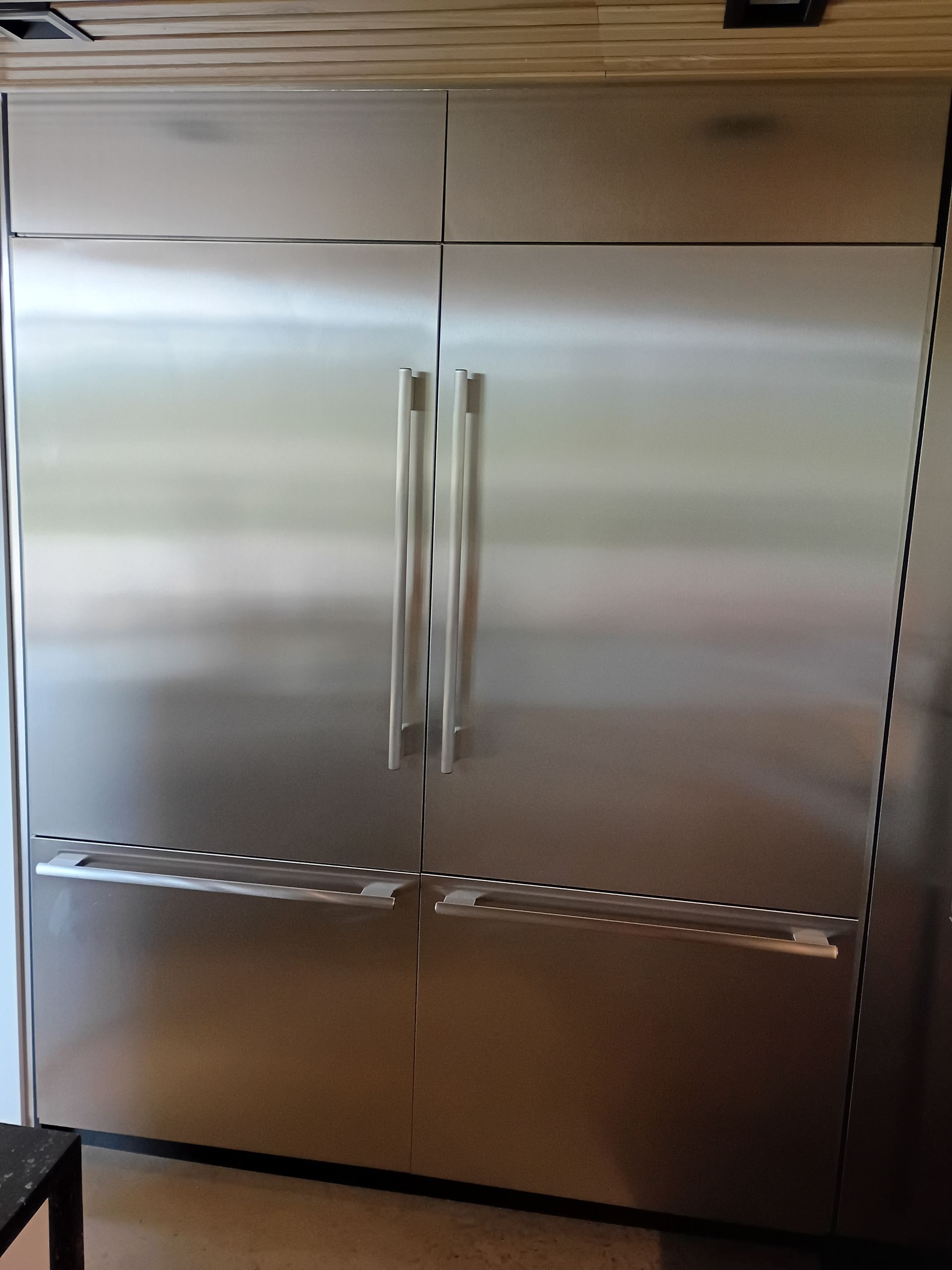 Stainless steel refrigerator with side-by-side doors and two bottom freezer drawers.