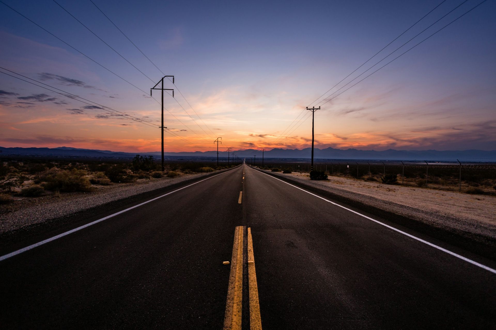 Road stretching into the distance at sunset with power lines along the road.