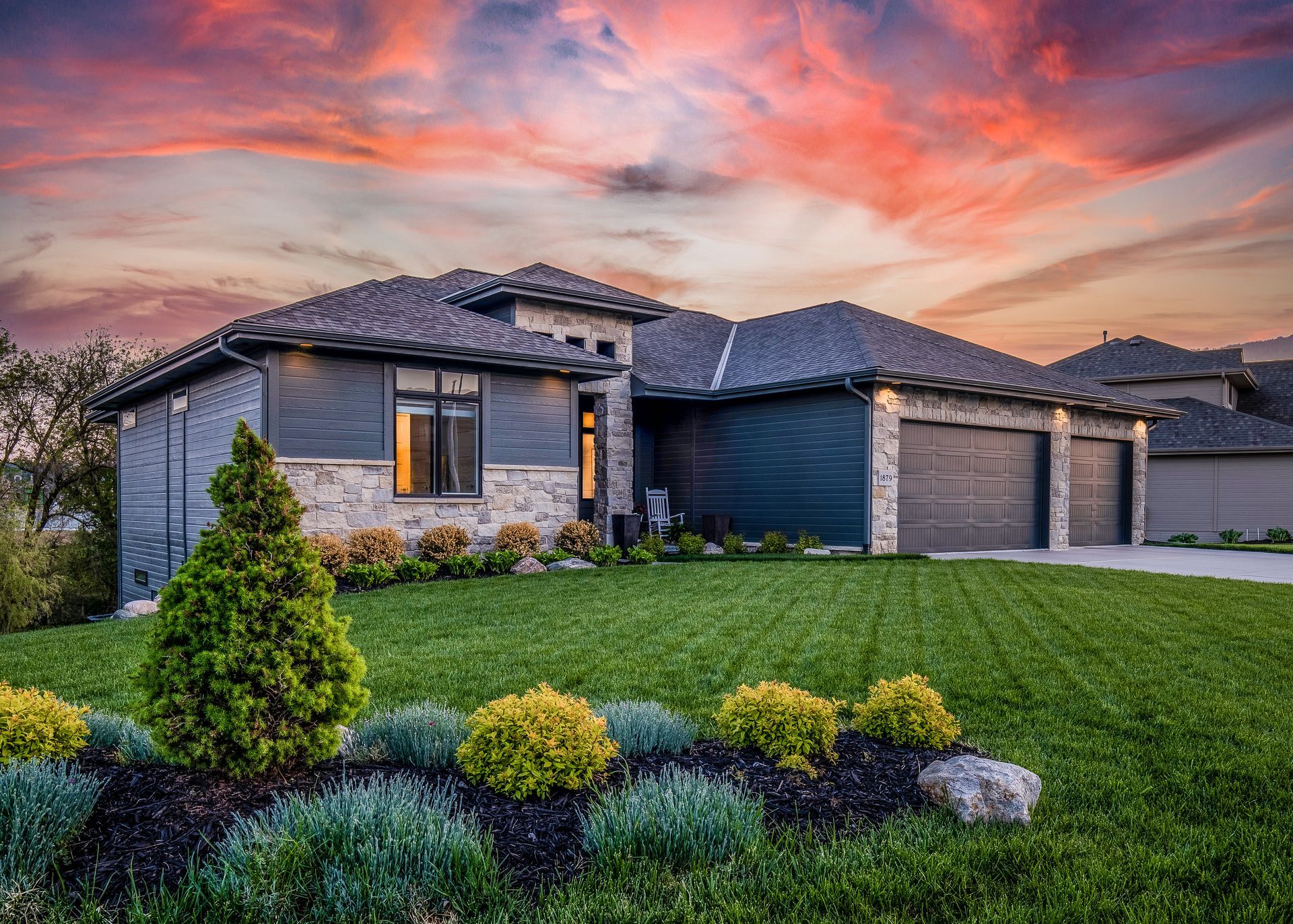 Beautiful modern home with landscaped front yard, green lawn, and colorful sunset sky.