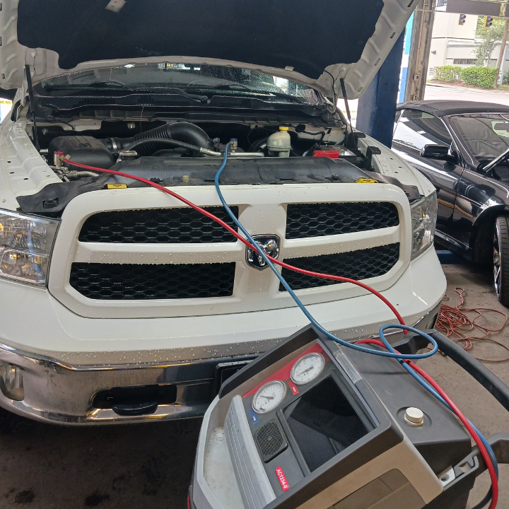 Truck in a repair shop with hood open, connected to a diagnostic machine by red and blue cables.