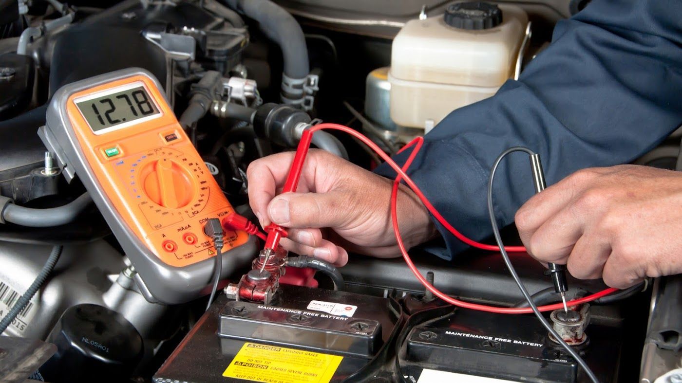 Mechanic testing a car battery with a multimeter and red probes under the hood