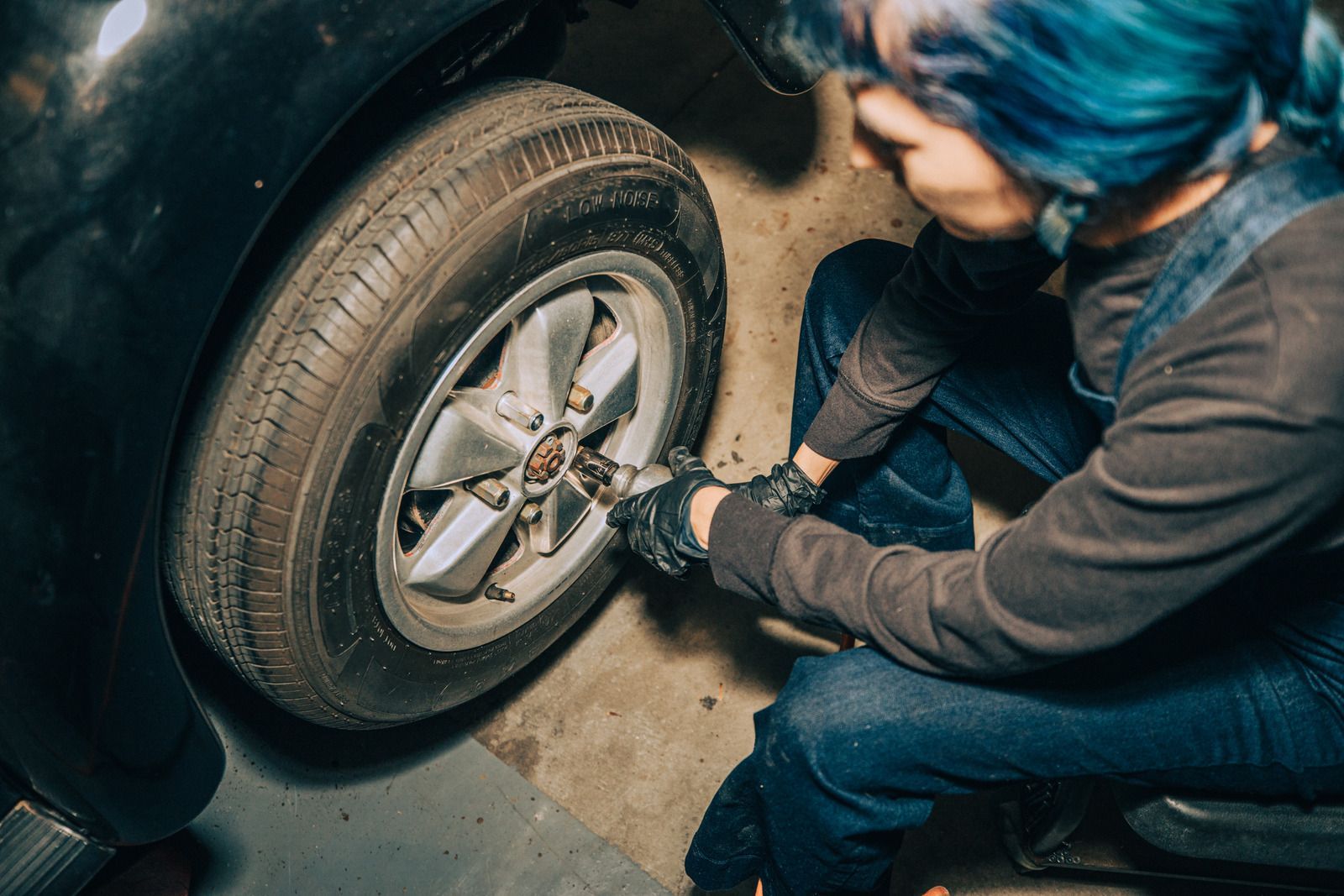 Person tightening a car wheel lug nut with a wrench beside a black tire