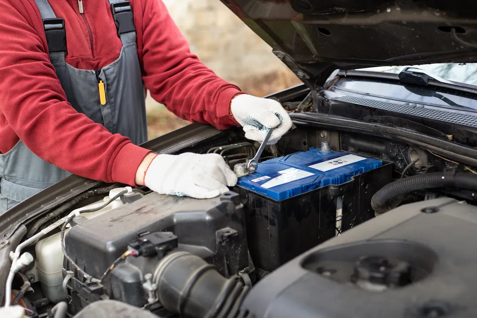 Mechanic wearing gloves checks a car battery under an open hood