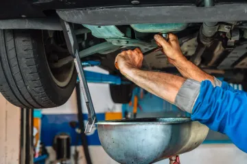 Mechanic working under a raised car, tightening parts into a large metal drain pan