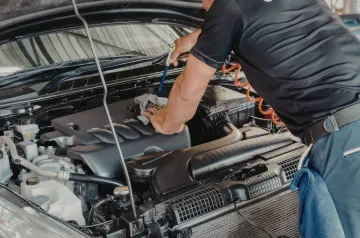 Mechanic working under an open car hood in a garage