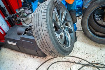 Car tire mounted on a wheel balancer in an auto repair shop, with tools and cables nearby