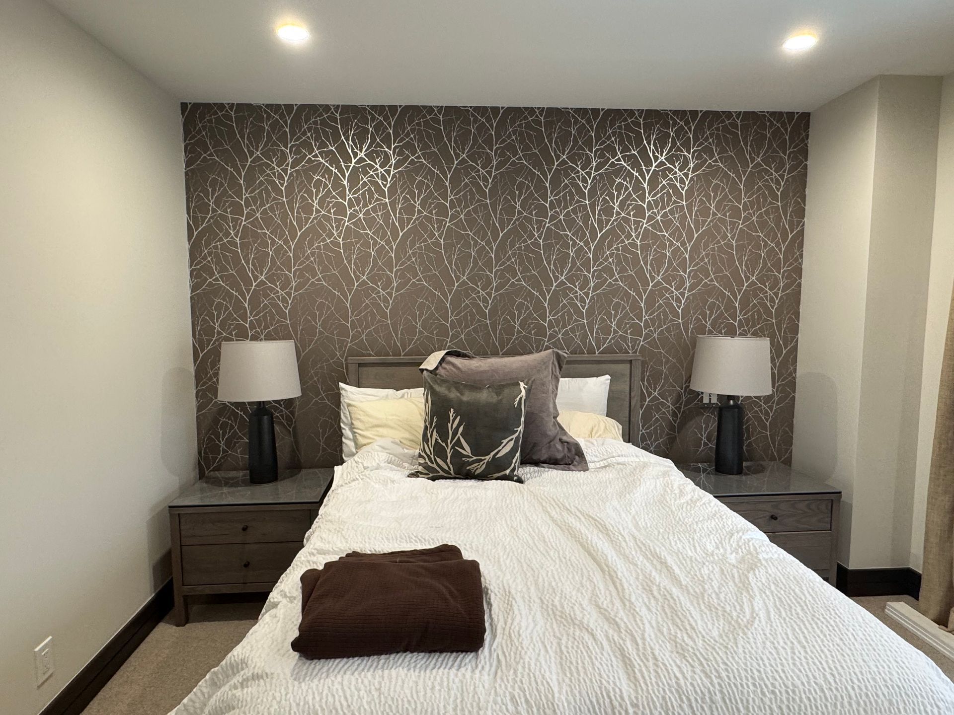 Neatly made bed in a modern bedroom with dark nightstands and patterned accent wall.