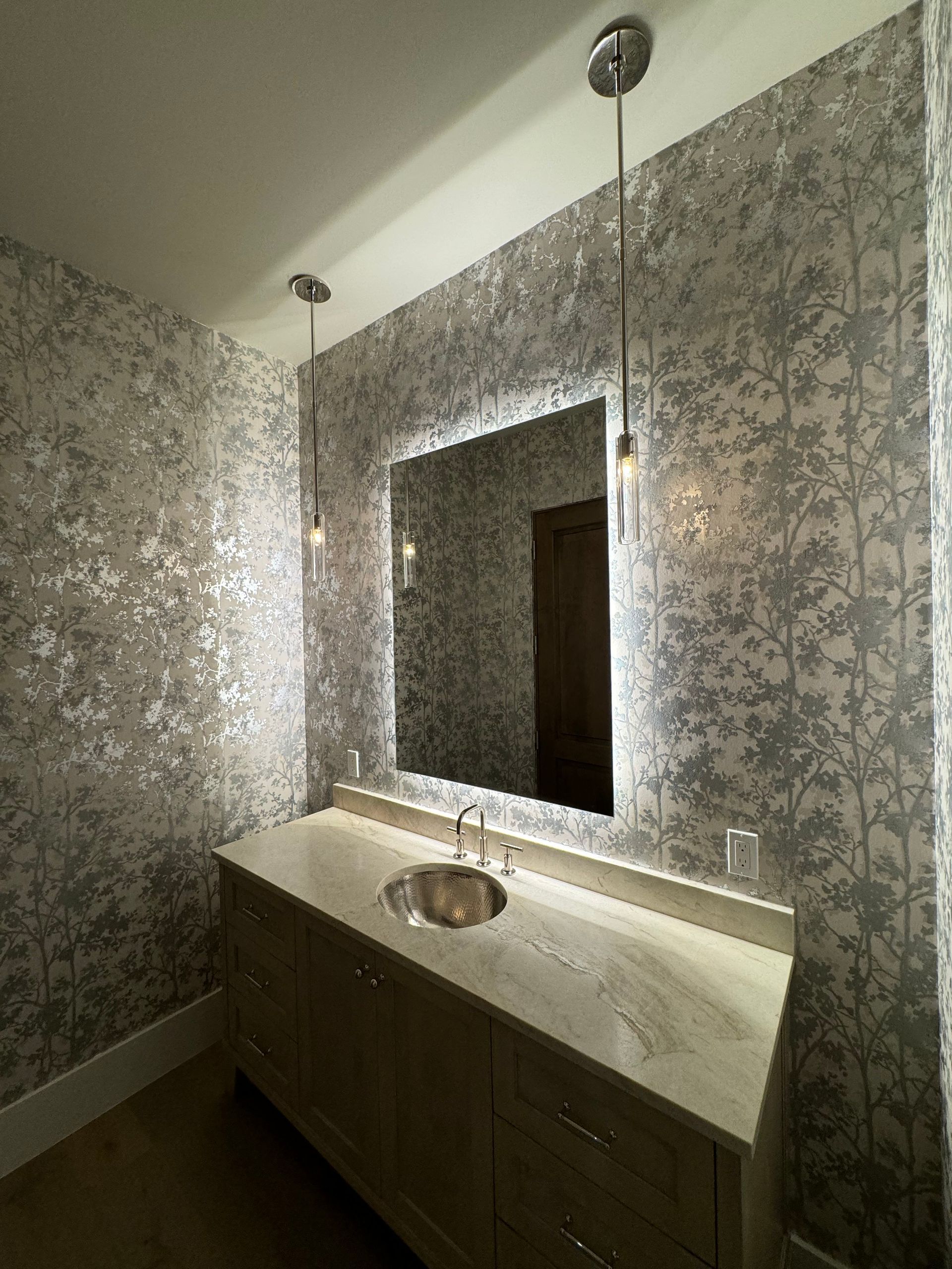 Modern bathroom vanity with mirror, pendant lights, and patterned wallpaper