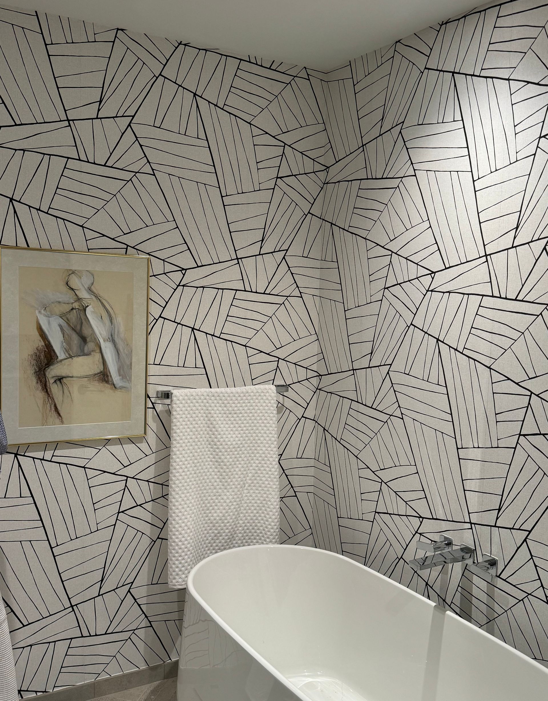 Modern bathroom with black-and-white patterned tile walls, a white tub, towel, and framed art.